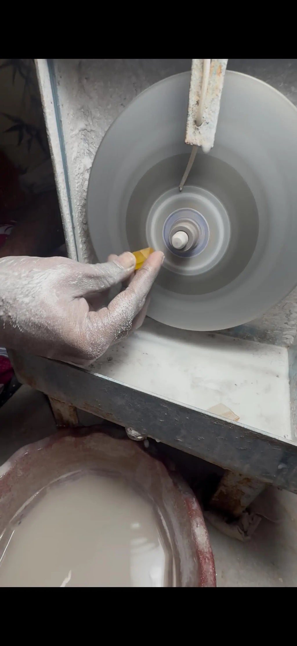 Hand grinding a gemstone on a rotating polishing wheel, stone held near disc