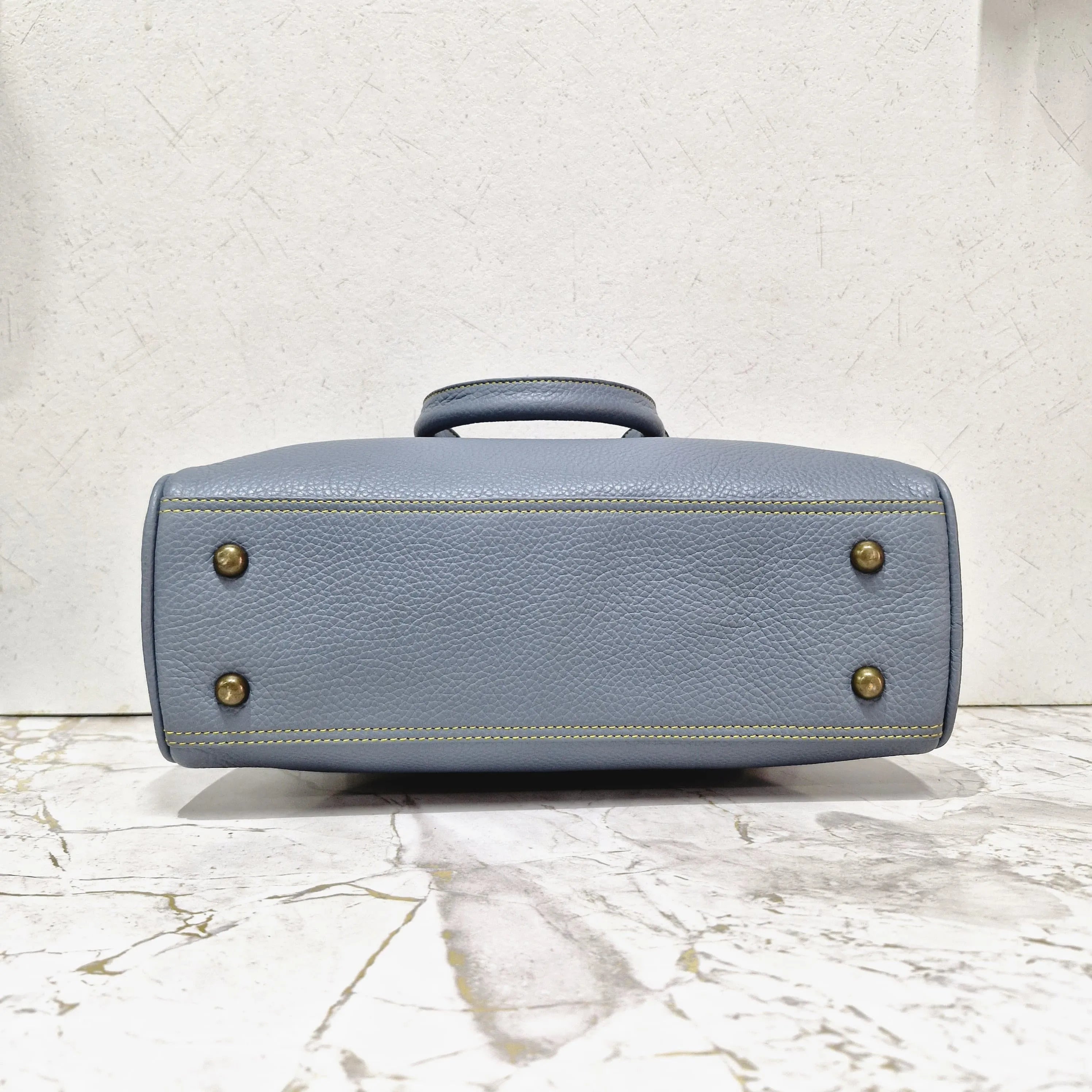 Blue pebbled genuine leather designer mini tote bag with gold metal feet and yellow contrast stitching.