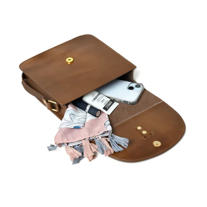 Brown leather crossbody designer handbag with gold button snap, open interior containing smartphone and tassel scarf.