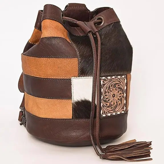 Brown and tan patchwork bucket bag with cowhide texture, floral embossed leather detail, drawstring, and tassel.