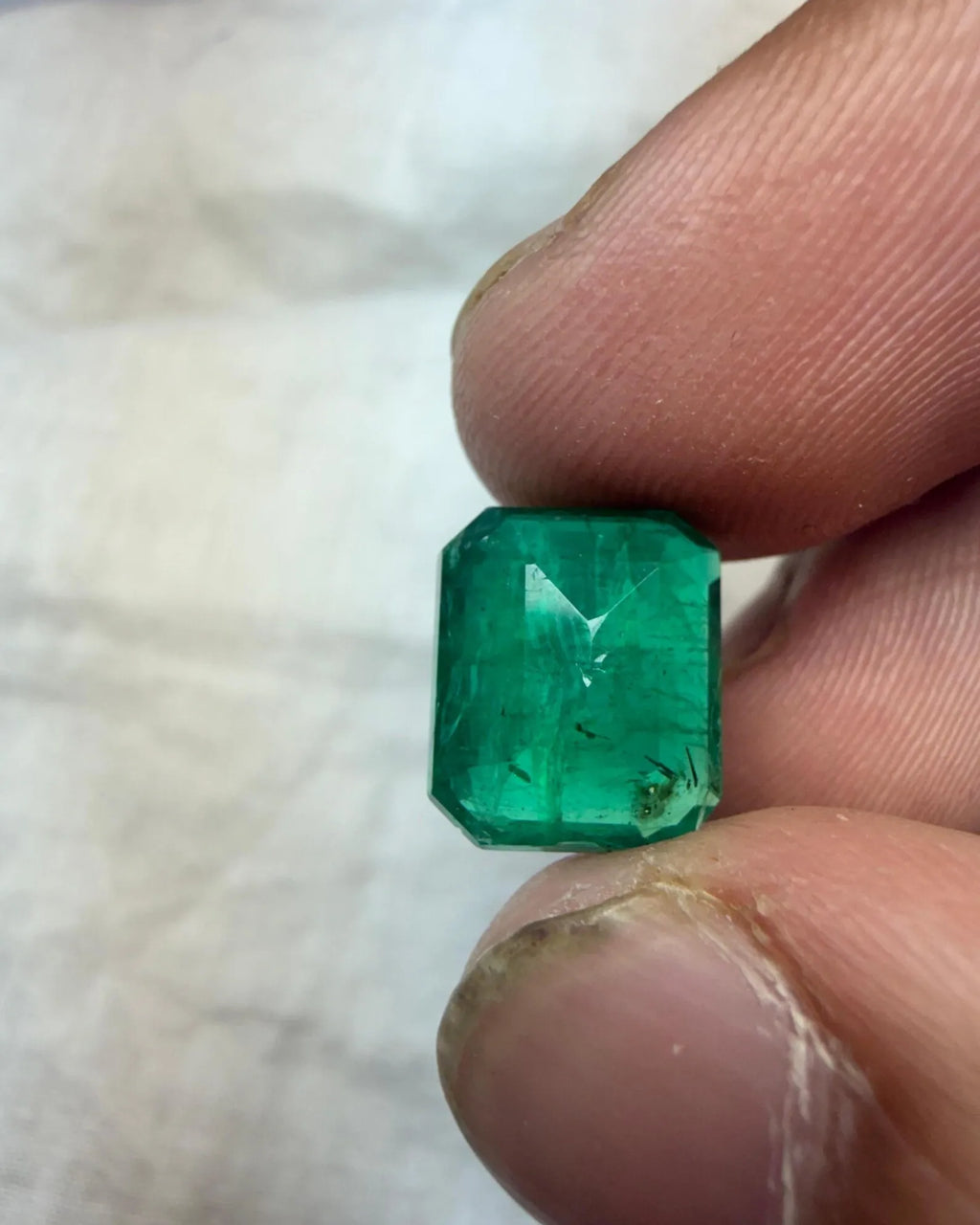 Green emerald-cut octagon gemstone close-up on fingers, facets and sparkle visible