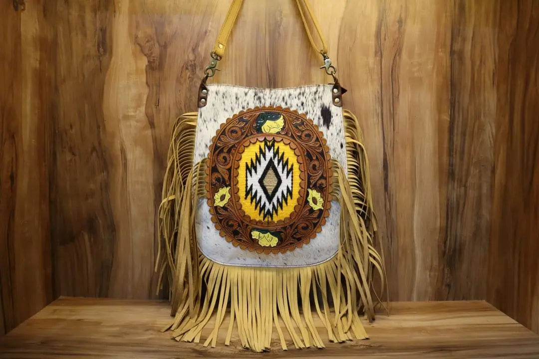 Handmade Western cowhide crossbody bag with tooled leather inlay, Aztec patterns, and long fringe trim.