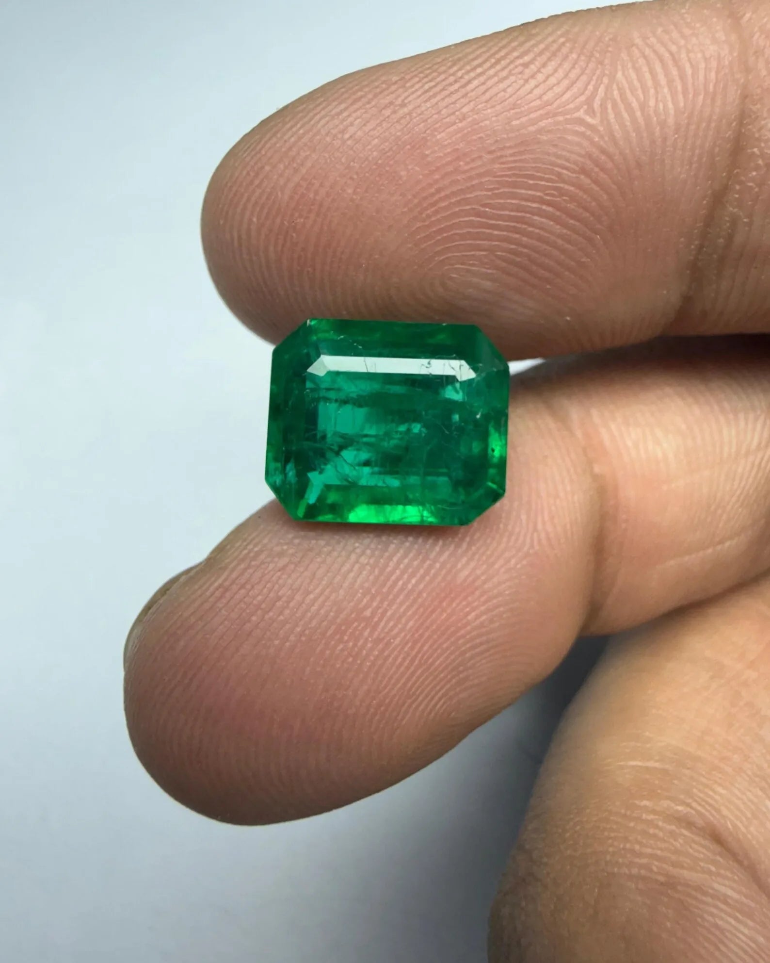 Green emerald-cut octagon gemstone held upright, sharp edges and facets visible
