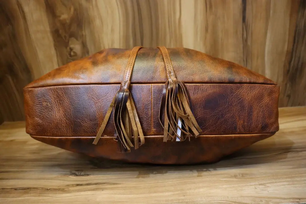 Distressed brown leather bucket shoulder bag with double tassel accents, casual bohemian style handbag.