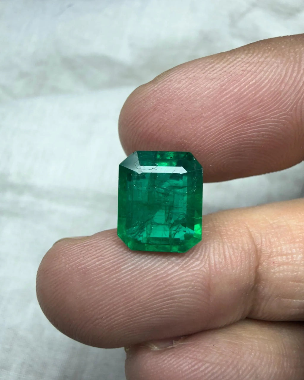 Green emerald-cut octagon gemstone centered on fingertip, clear facet lines visible