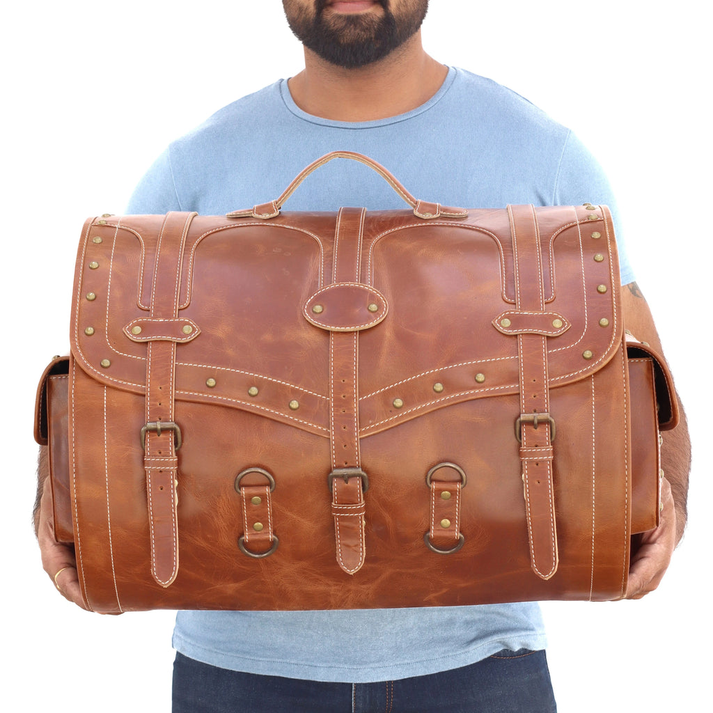 Large vintage brown leather trunk bag for travel with brass buckle straps, rivet detailing, and heavy-duty top handle.
