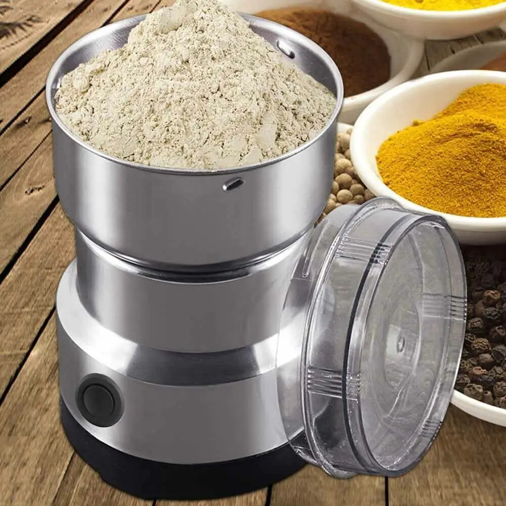 Stainless steel electric spice and coffee bean grinder with clear lid, filled with ground powder on wooden table.
