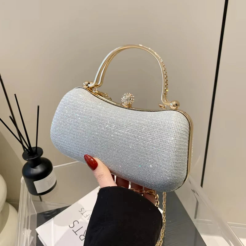 Silver glitter evening clutch with crystal top handle, gold hardware, and rhinestone clasp for wedding or parties.