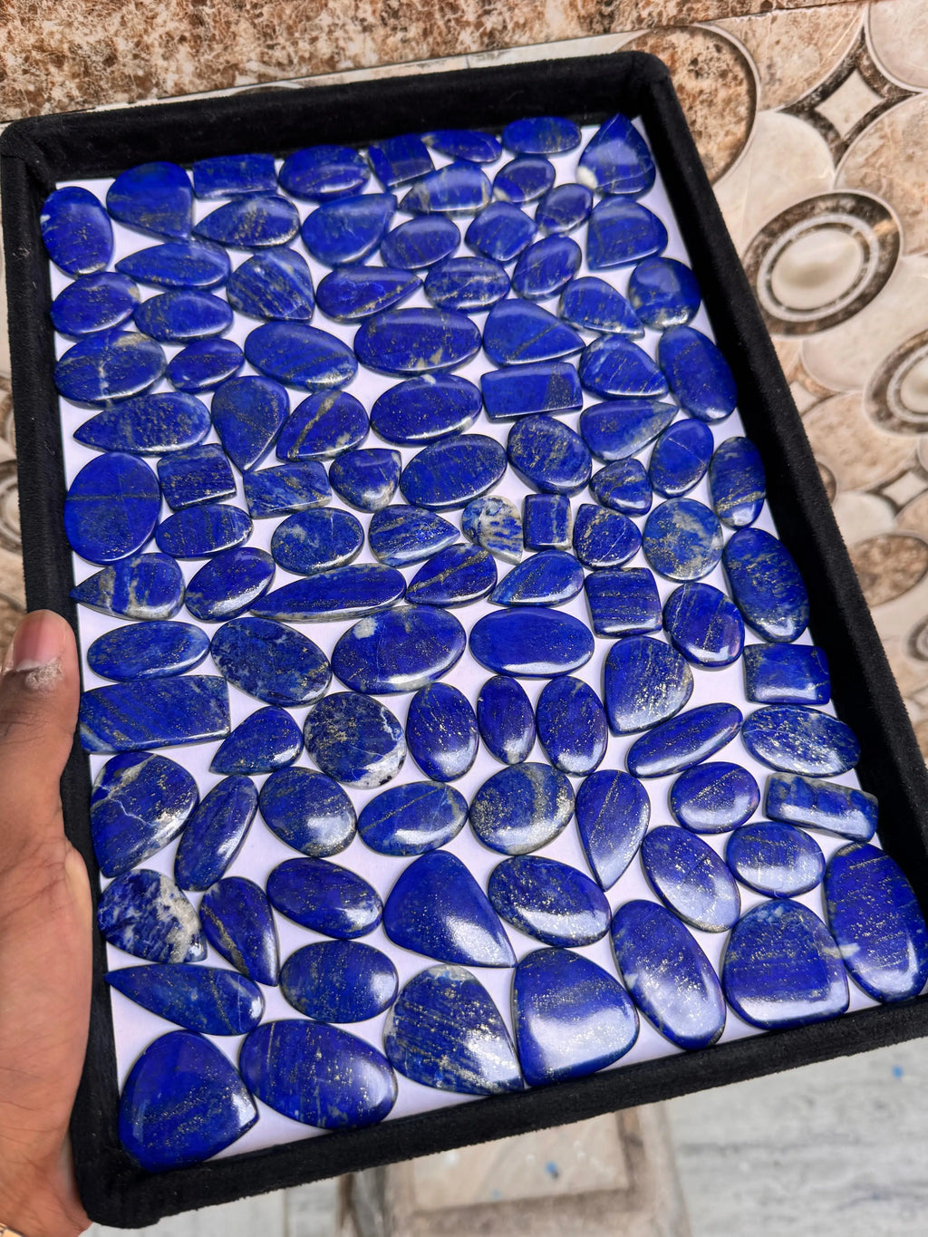 Lapis lazuli cabochon gemstone assortment in a black tray, blue ovals and rounds