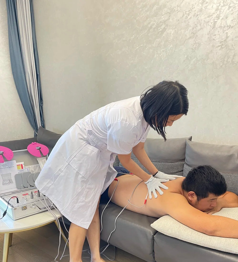 Therapist using a silver DDS bioelectrical body therapy massager device on a man's back for home electrotherapy.