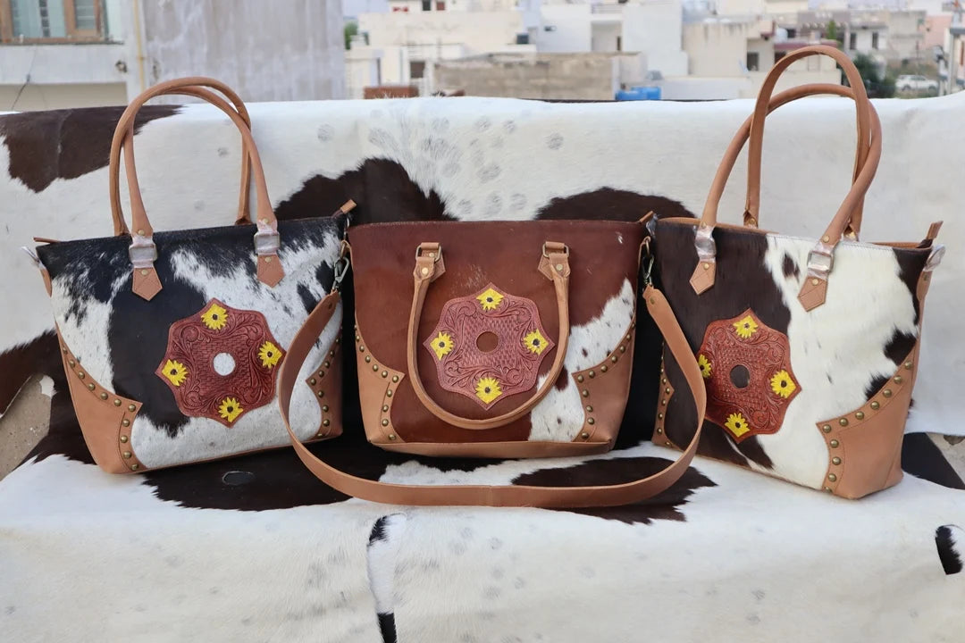 Three western fur leather handbags with tooled floral patches, brown animal prints, tan leather trim, and dual straps.
