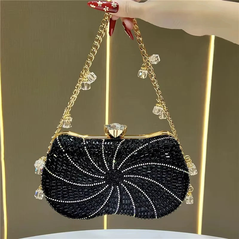 Black crystal-embellished evening clutch with gold chain strap, rhinestone swirls, and crystal charms. Designer handbag.