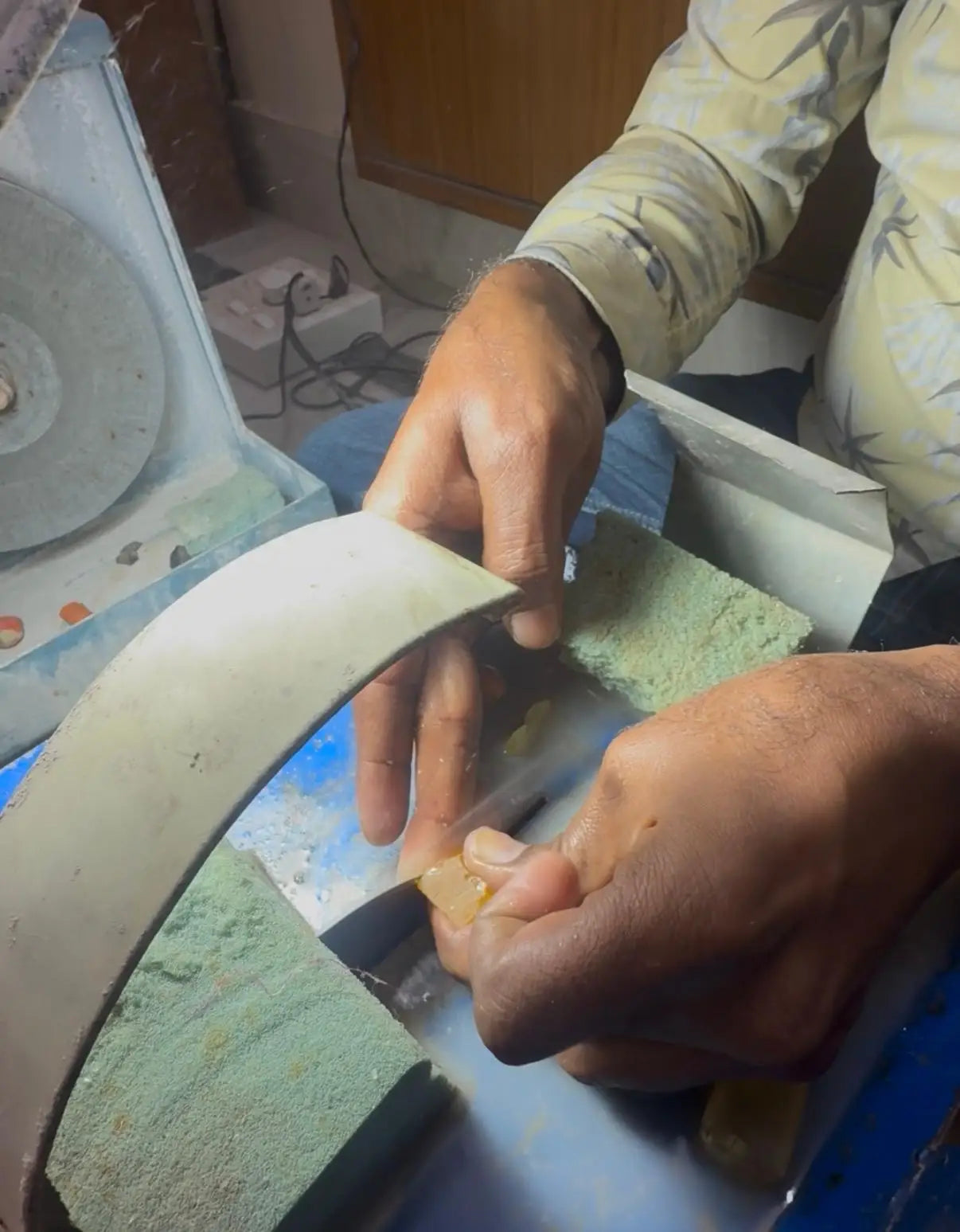 Hands working on a gemstone piece at the grinding wheel, small fragments visible