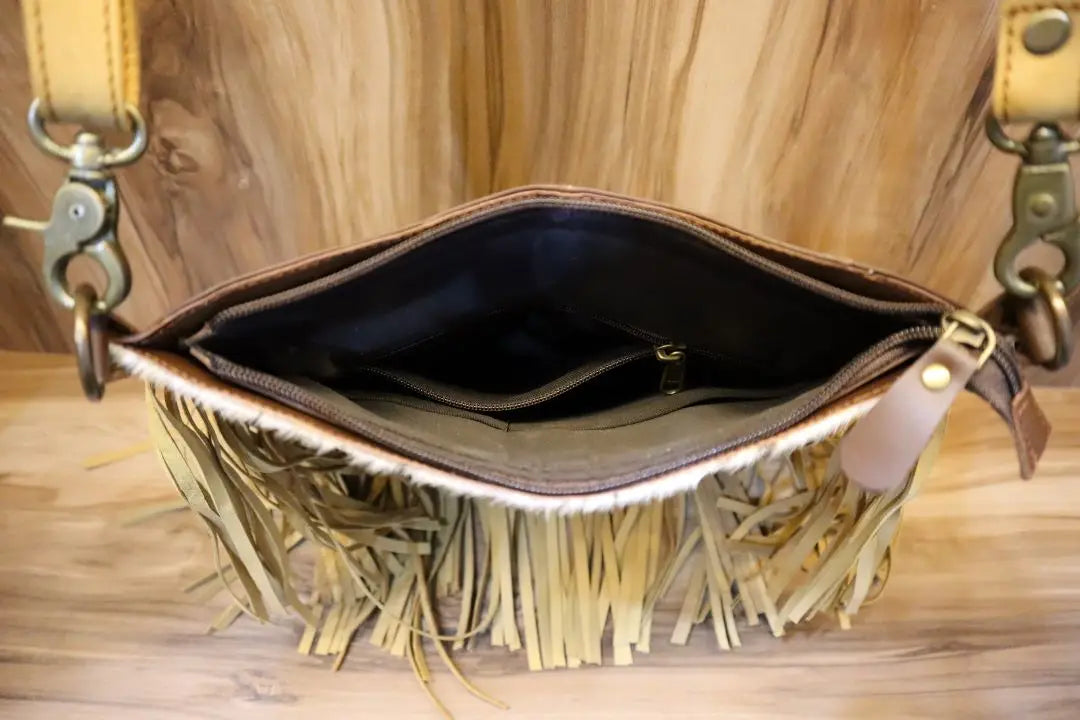 Tan leather fringe crossbody bag with top zipper closure, fabric lining, and metal clasps, viewed from above.