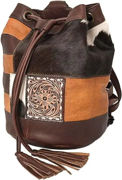 Western bucket bag in multi-tone leather and cowhide with embossed floral patch, drawstring closure, and fringe tassel.