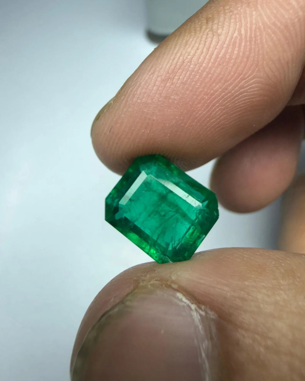 Green octagon-cut emerald gemstone close-up, faceted surface held between fingers