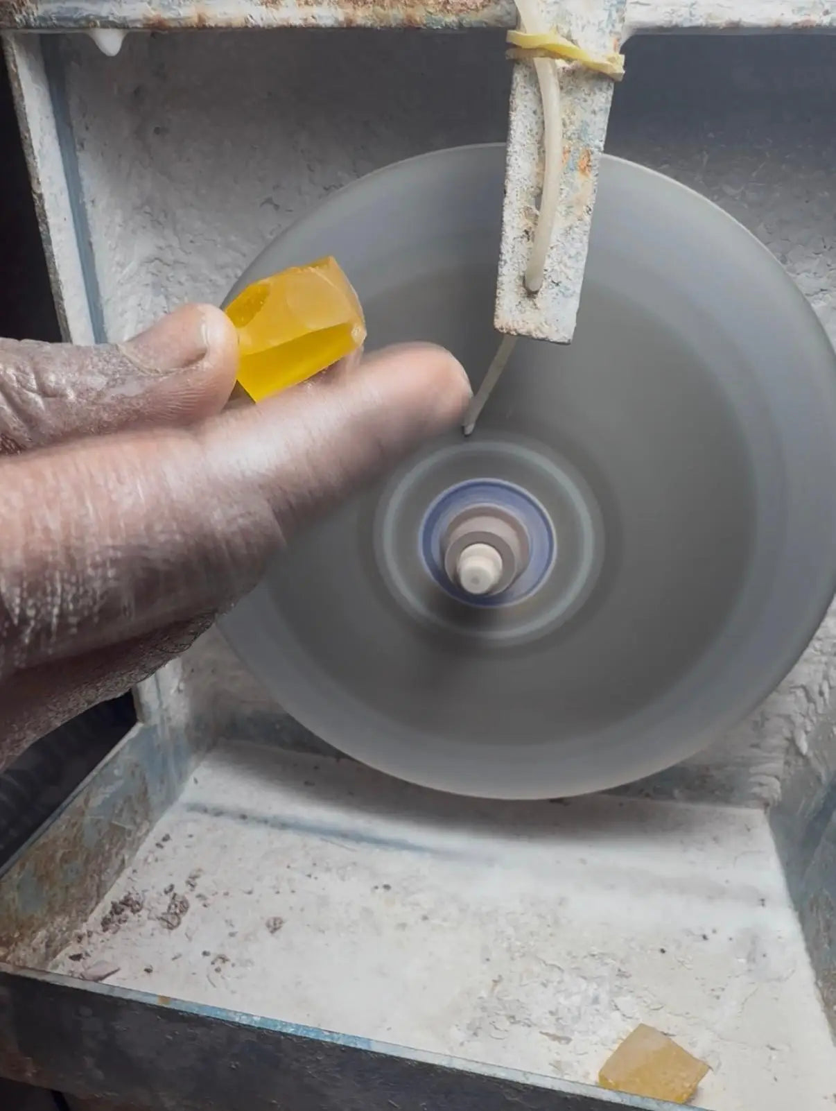 Small yellow gemstone piece held near a rotating grinding wheel