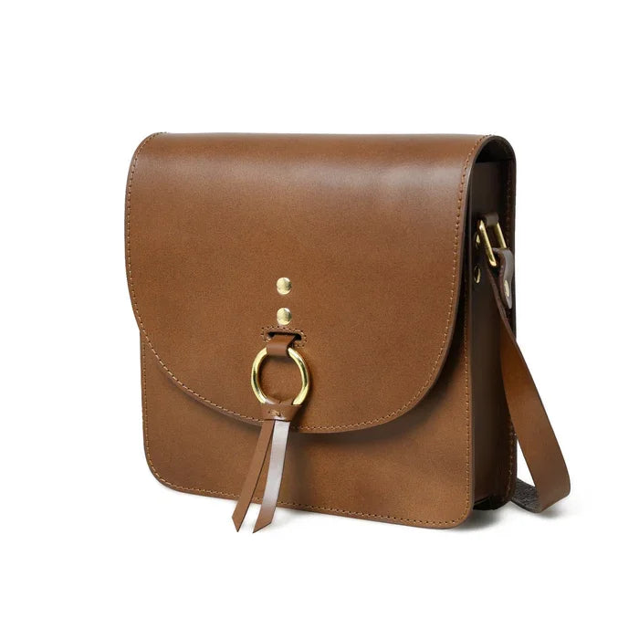 Tan leather designer crossbody bag with gold ring closure and minimalist flap style.