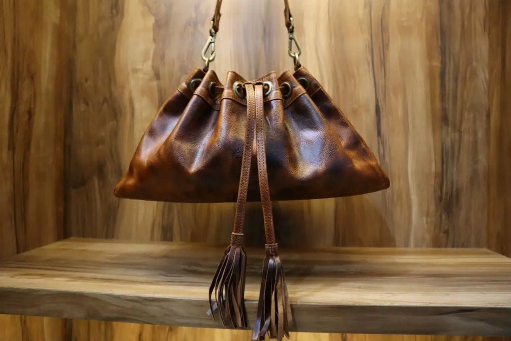 Brown distressed leather bucket shoulder bag with drawstring closure, metal hardware, and tassel accents. Trunk style.