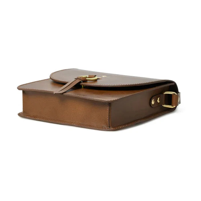 Brown leather designer crossbody bag with a round gold buckle, minimalist flap closure, and polished gold hardware.