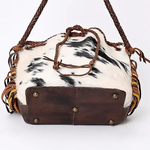 Vintage cowhide bucket bag, brown leather base, braided straps, fringe, and drawstring closure. Trendy boho trunk style.