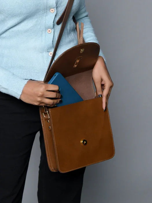 Tan leather designer crossbody bag with gold hardware, minimalist flap closure, and adjustable shoulder strap.