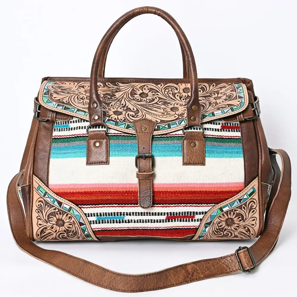 Handwoven western leather duffel trunk with floral tooling, colorful striped textile, and adjustable shoulder strap.