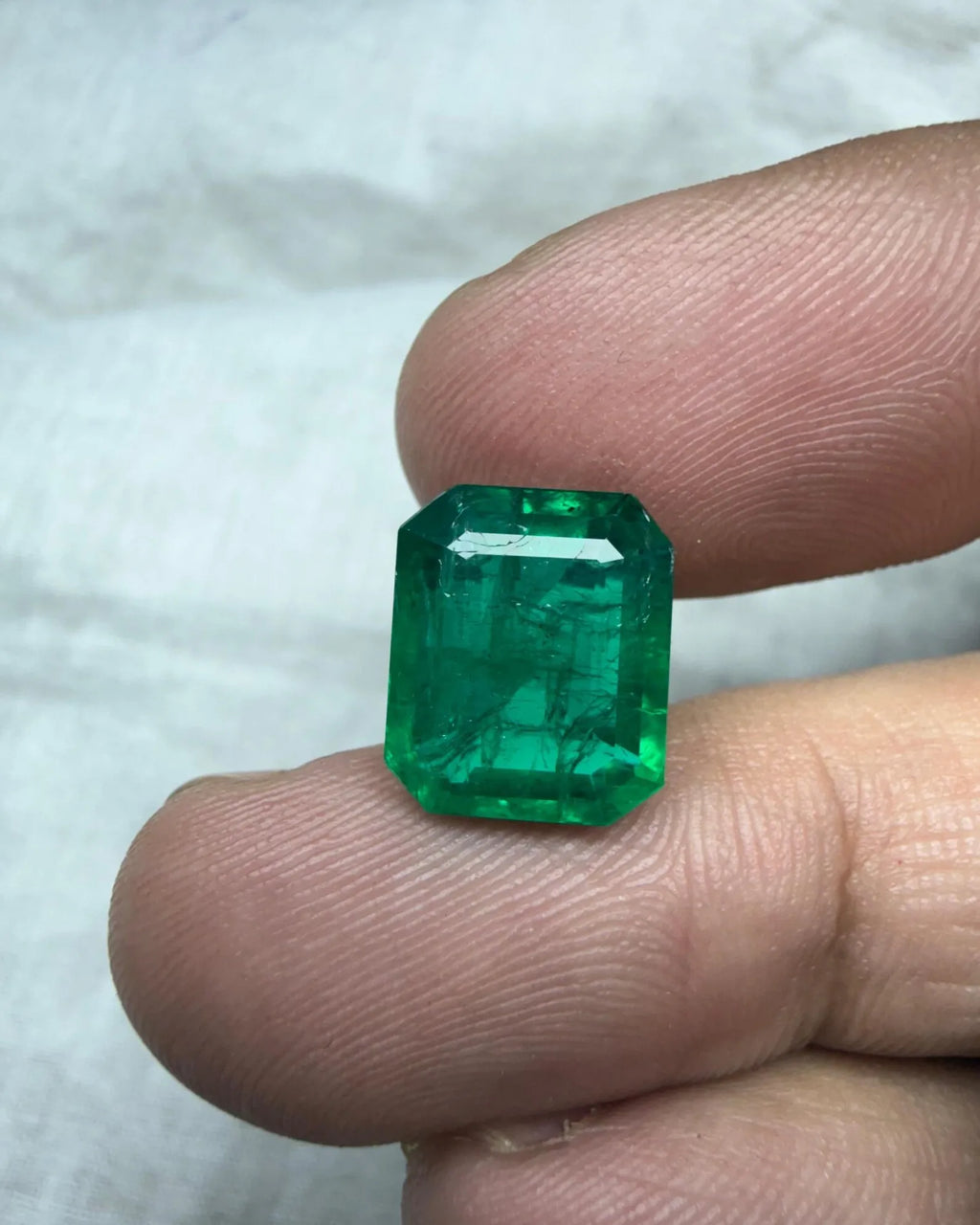 Green octagon-cut emerald gemstone on fingertip, bright faceted surface