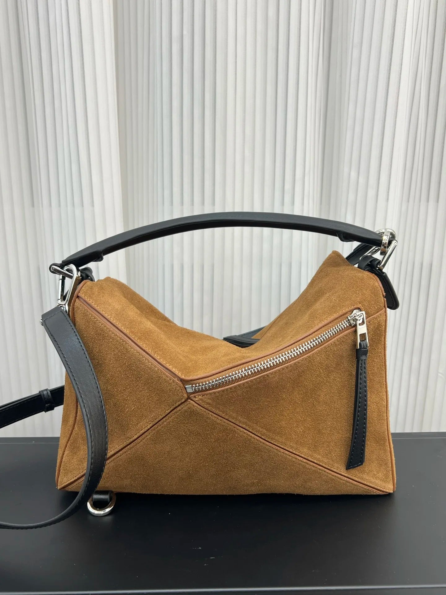 Brown suede designer crossbody bag with black leather handle, geometric paneling, and silver zip detailing.