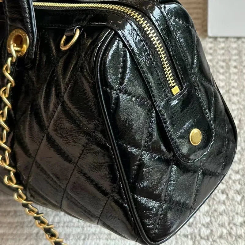 Black shiny quilted patent leather barrel satchel with gold chain strap and hardware. Designer handbag.