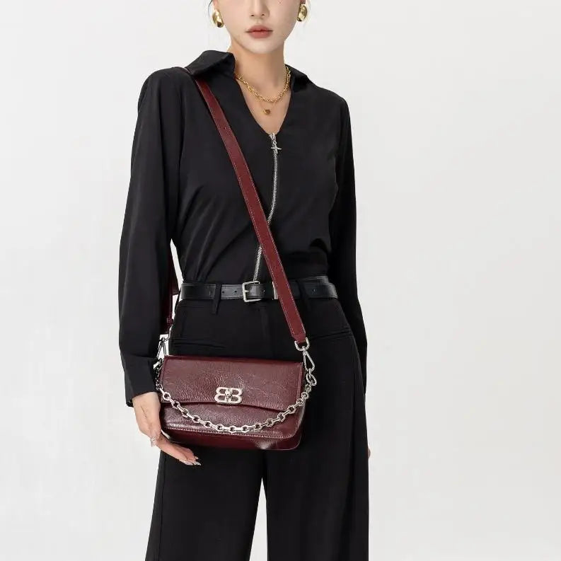Burgundy leather shoulder bag with chain strap and metallic logo, worn as a stylish designer clutch.