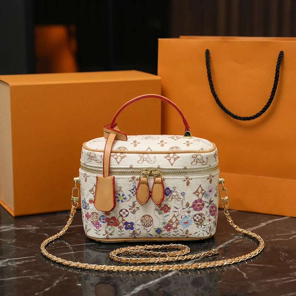 Luxury cowhide vanity trunk bag with multicolored floral monogram print, red leather handle, and gold chain strap.