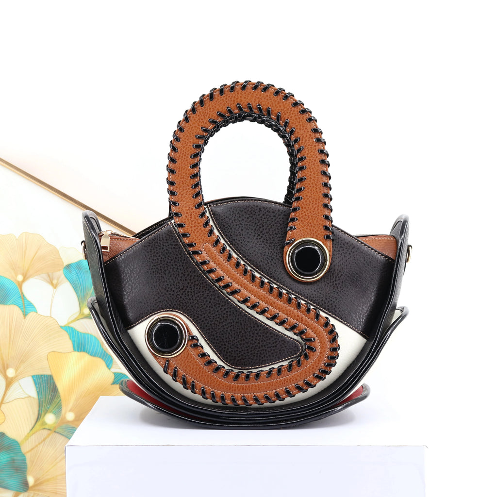 Designer handbag with unique curved tan and black leather design, bold stitching, and large circular grommet accents.