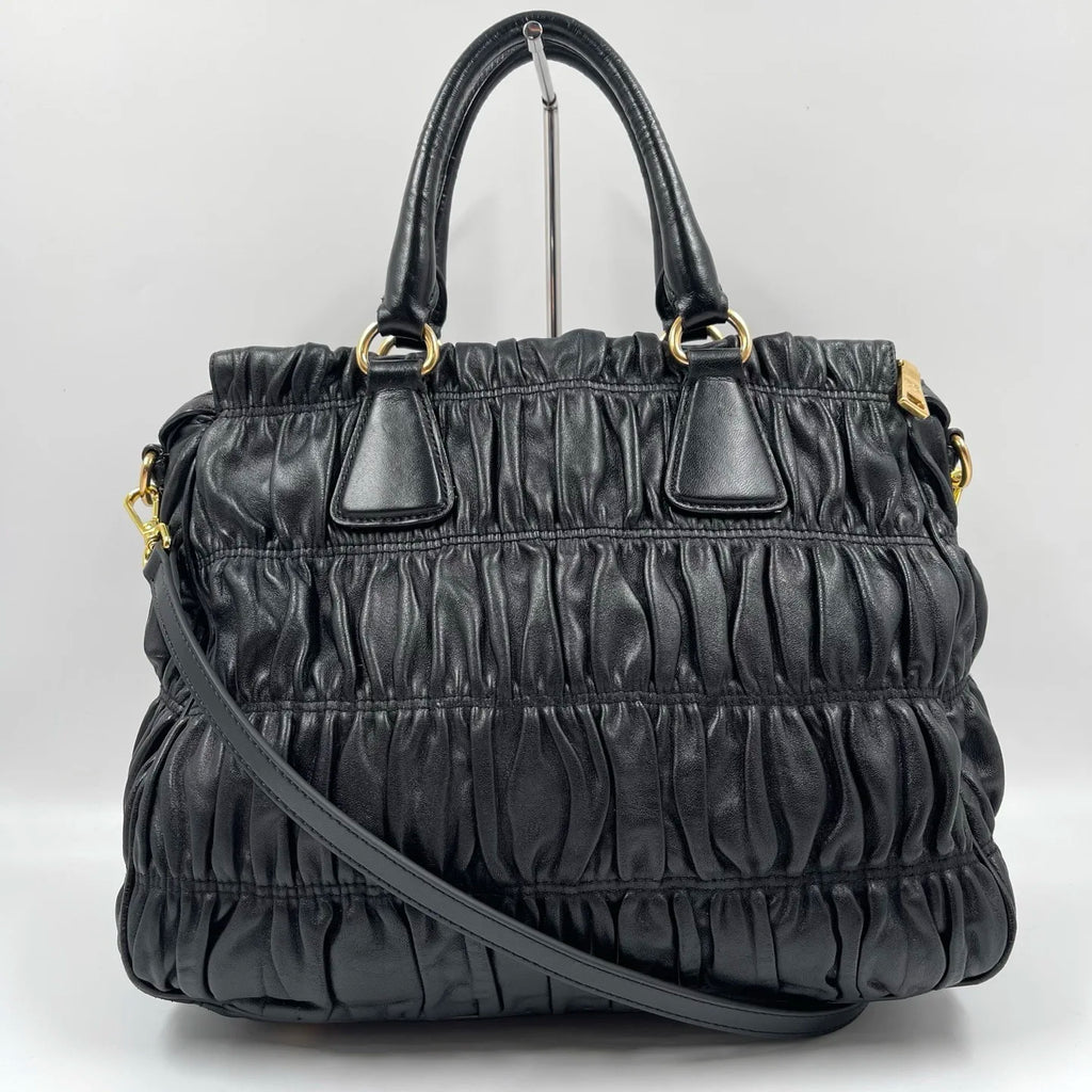 Luxury black pleated leather designer handbag with gold hardware, top handles, and detachable crossbody strap.