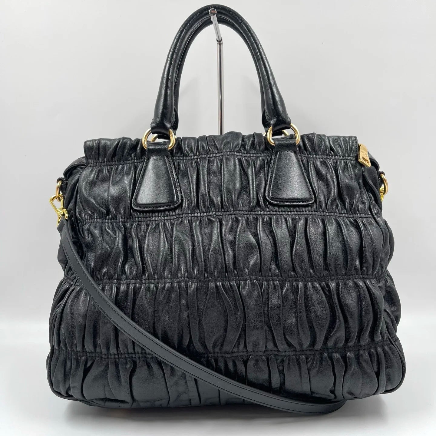 Luxury black pleated leather designer handbag with gold hardware, top handles, and detachable crossbody strap.
