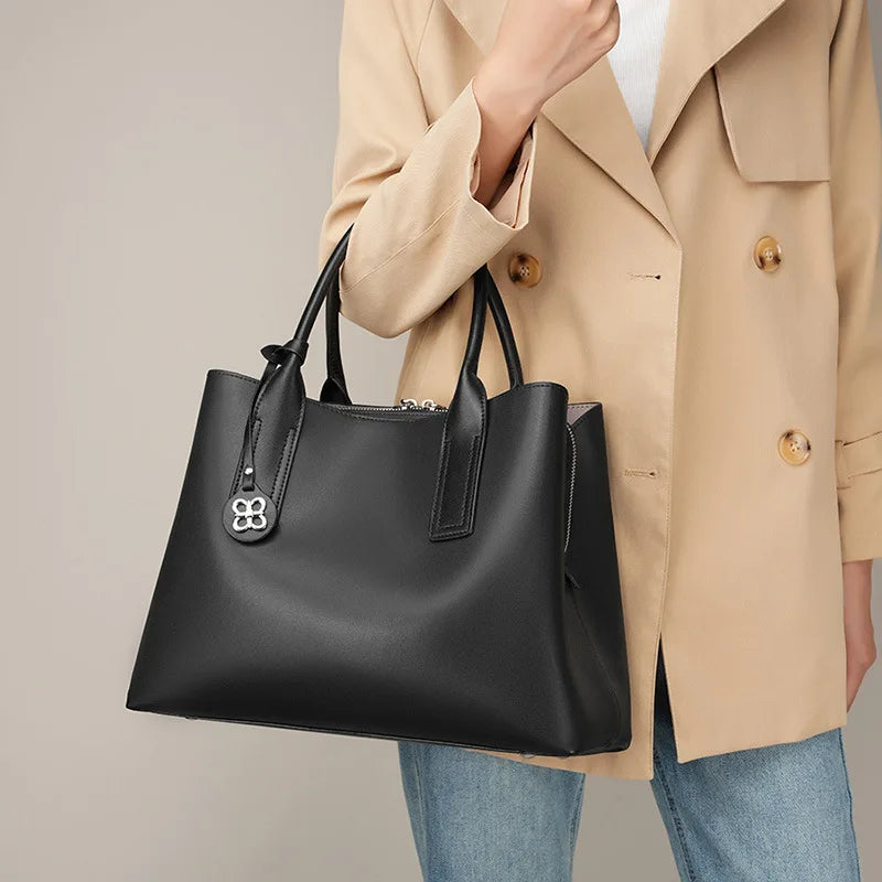 Elegant black genuine leather large capacity designer handbag with zipper closure and dangling silver logo charm.