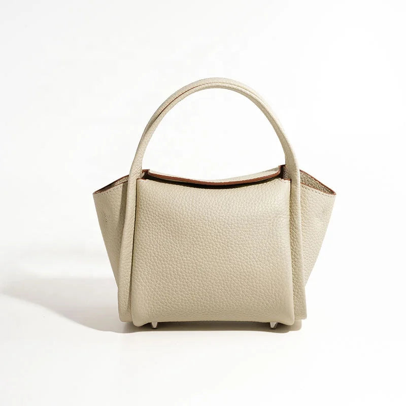 Beige pebble leather designer handbag with a structural yuanbao shape, top handle, and minimalist casual style.