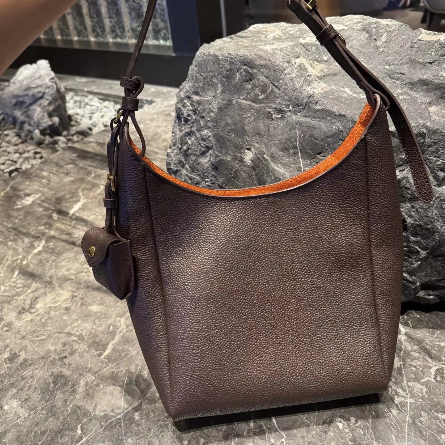 Brown genuine leather hobo bag with adjustable shoulder strap, gold hardware, and vibrant orange interior lining.