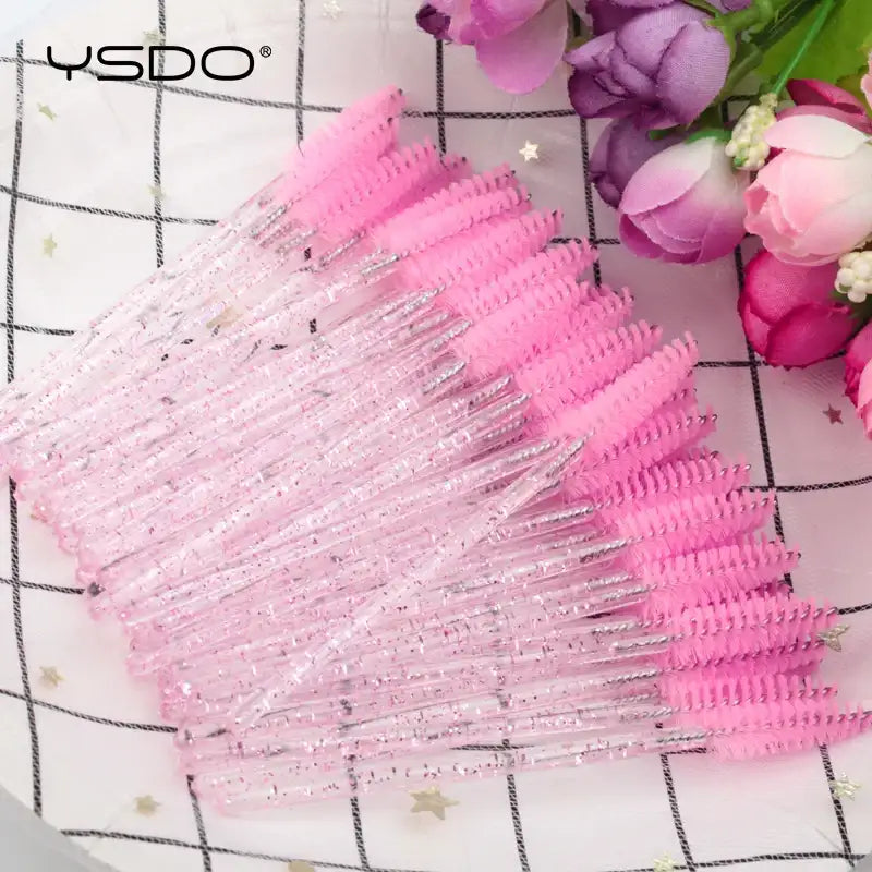 Disposable mascara wands with pink bristles and glittery, transparent plastic handles for grooming lashes and brows.