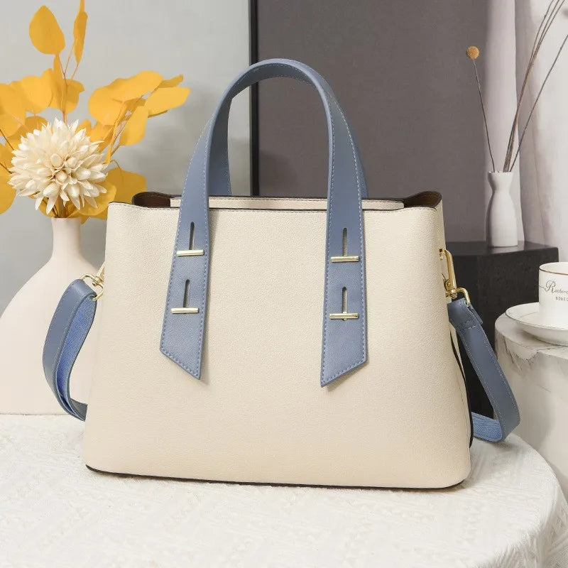 Cream leather designer handbag with blue handles, gold bar accents, and detachable crossbody strap.