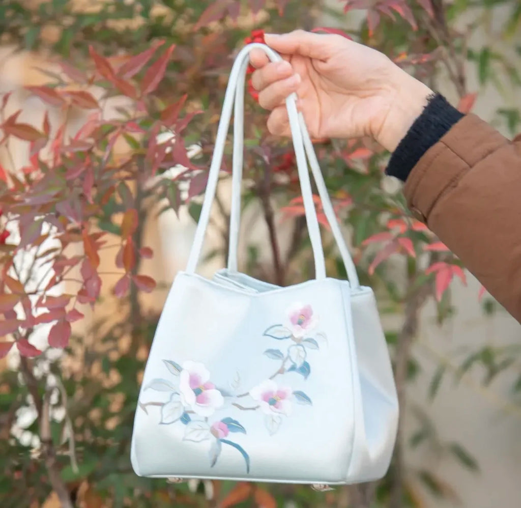 Handmade light blue silk handbag featuring elegant Suzhou embroidery of delicate pink flowers and leaves.