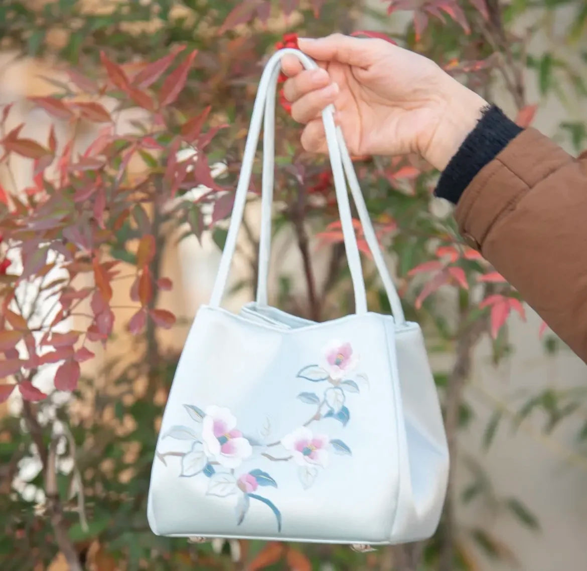 Handmade light blue silk handbag featuring elegant Suzhou embroidery of delicate pink flowers and leaves.