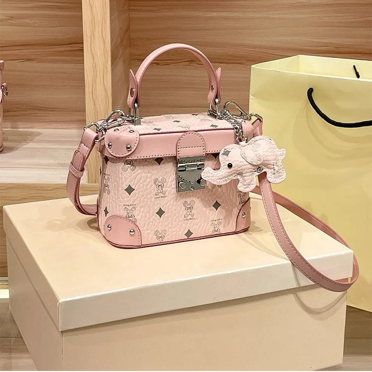 Pink cowhide trunk handbag with minimalist print, top handle, shoulder strap, and cute elephant charm.