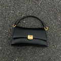 Black designer underarm handbag with gold magnetic clasp, square structure, and dual-ring strap attachment.