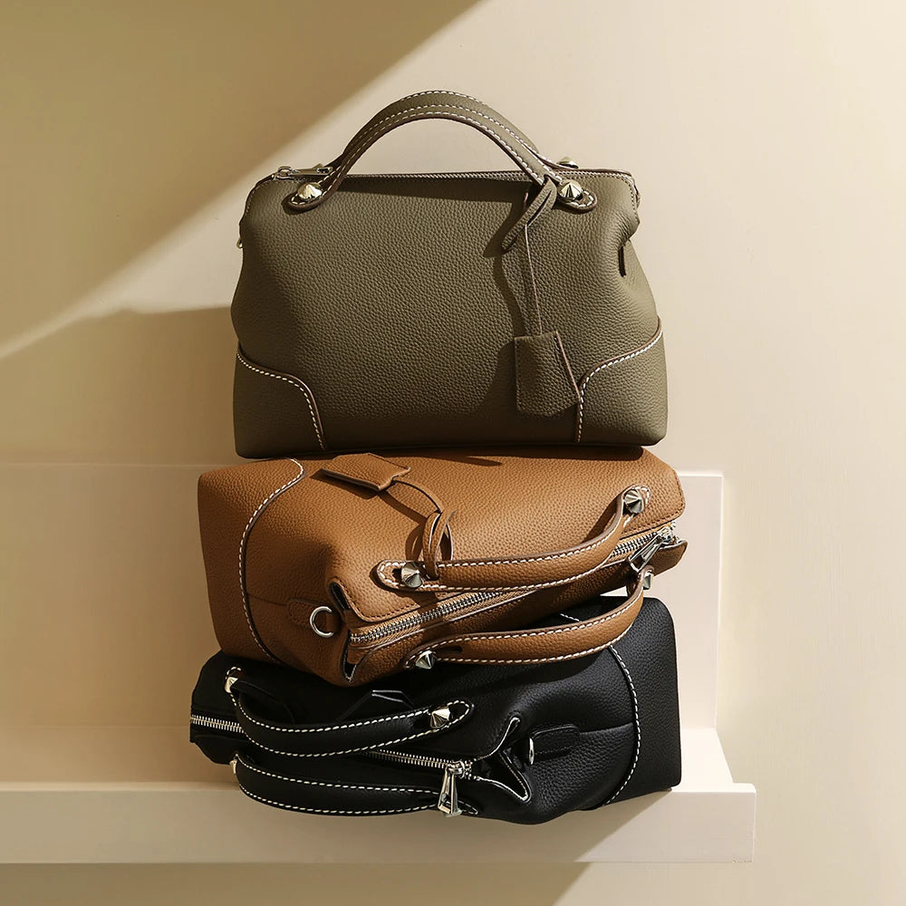 Stacked olive, brown, and black designer handbags in pebbled top-grain cowhide leather with contrast stitching.