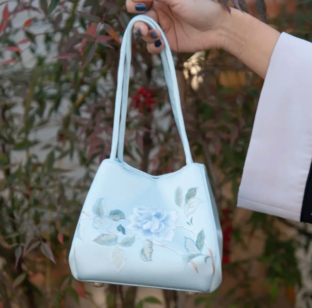 Light blue silk designer handbag with delicate floral Suzhou embroidery and structured handles.
