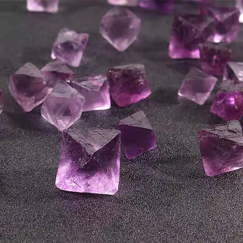 Purple rough crystal octahedra, scattered on dark tabletop, faceted points and chunks