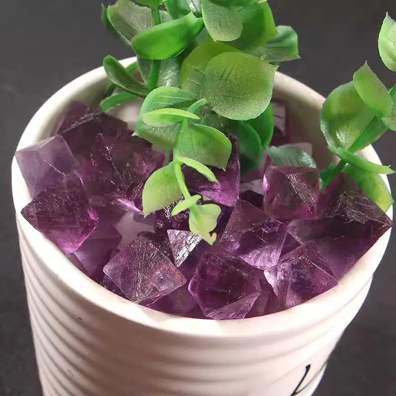 Purple rough crystal octahedra in white pot, scattered faceted chunks with glossy faces
