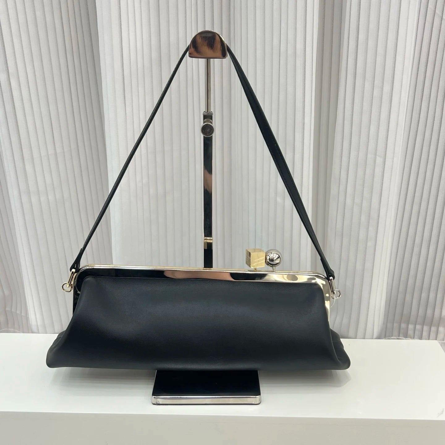 Black leather shoulder bag, designer handbag with gold metal frame, clip closure, and sleek rectangular silhouette.