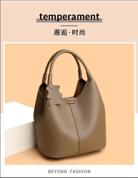 Taupe pebbled leather bucket handbag, casual commuter style with top handles and a decorative bear charm.